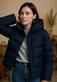 Donkerblauwe pufferjack met een capuchon, voorzien van geëmailleerde secties en een ritssluiting. Draag het over een grijs T-shirt, in combinatie met blauwe jeans.