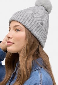 Gorro de punto gris con un patrón texturizado y un pompón esponjoso en la parte superior. Presenta detalles acanalados y tela suave.