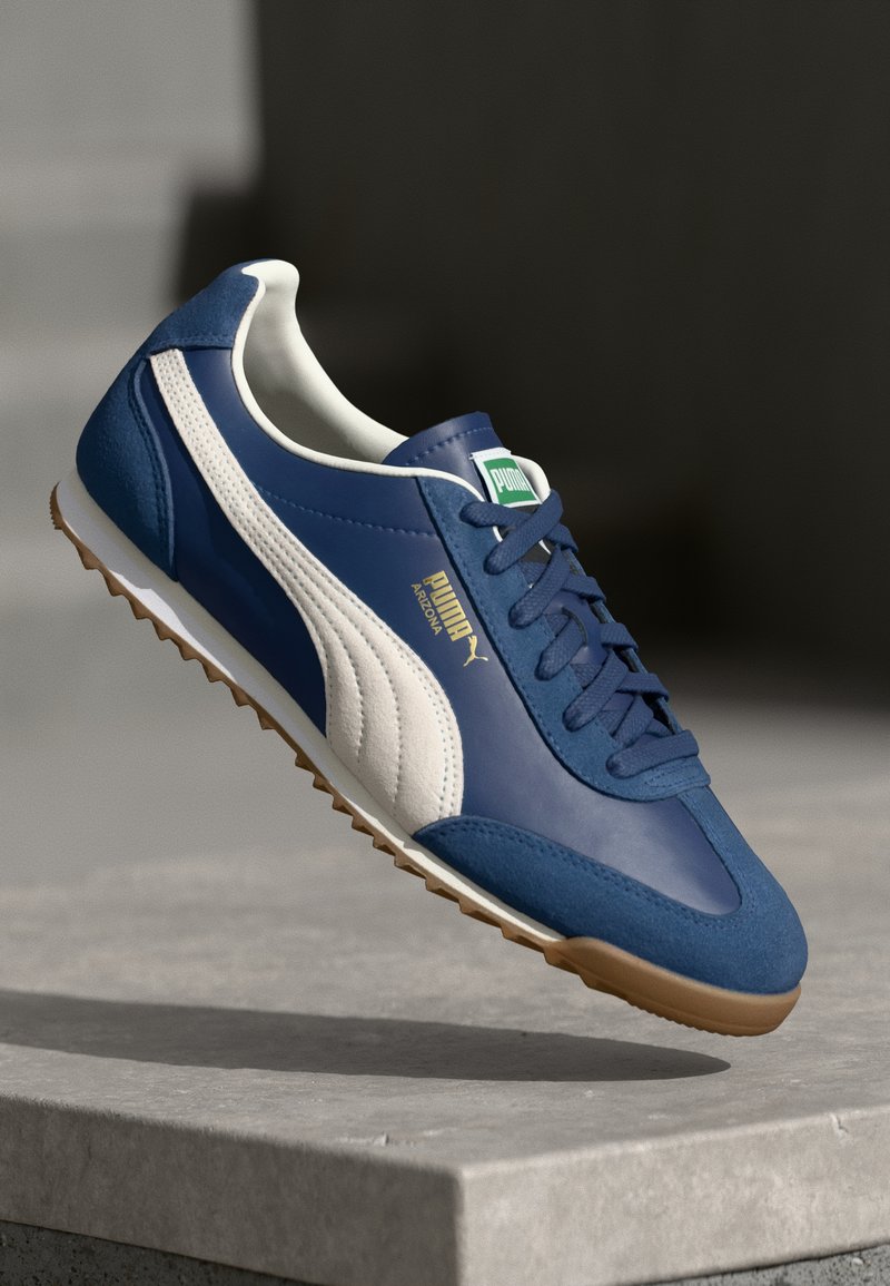 Plave i bijele tenisice, izrađene od antilopa i kože, s okruglim vrhom, teksturiranom potplatom i kontrastnim potplatom od gume. Vidljiv PUMA logo.