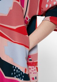 Tissu coloré avec des motifs abstraits en rose, rouge, bleu et noir. Coupe ample avec manches larges, texture lisse et tombé confortable.