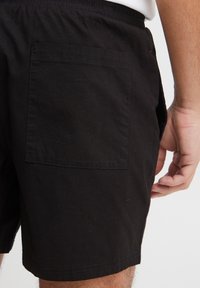 Mustad puuvillased lühikesed püksid elastse vöökohaga, millel on üks tagatasku ja sirge lõige. Sile tekstuur ilma mustriteta.