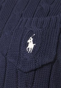 Navy knitted sweater featuring a textured cable pattern, with a white embroidered polo logo on the chest pocket.
