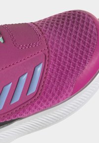 Zapatilla deportiva rosa con una parte superior texturizada, que presenta acentos de malla y lisos. Incluye una correa de velcro y una suela de goma blanca con ranuras.