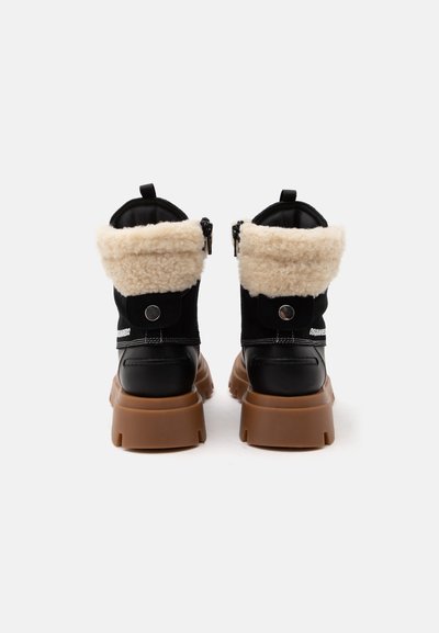 Paire de bottines noires avec semelles épaisses marron et revers en peau lainée beige, vues de dos sur fond blanc.
