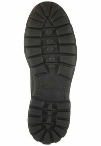 Suela de zapato de goma negra con una superficie rugosa y texturada. Presenta un patrón de tacos profundos y un logo grabado cerca del talón para mayor agarre y estabilidad.