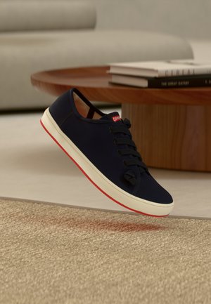 Marineblaue Segeltuch-Sneaker mit schwarzen Schnürsenkeln, weißer Zwischensohle und roten Akzenten an der Laufsohle, ausgestattet mit einer abgerundeten Spitze und strukturierter Oberfläche.