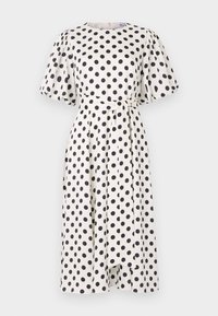 Vestido branco com bolinhas pretas, mangas curtas e bufantes, decote redondo e um cinto correspondente na cintura. O tecido parece suave e leve.