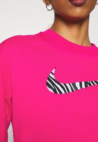 Rosa långärmad sweatshirt med en svartvit zebramönstrad Nike-logotyp på framsidan. Slät textur, rundhalsad design.