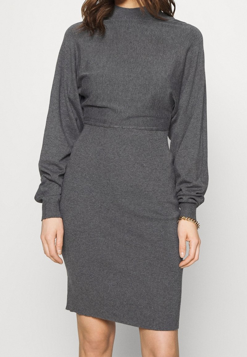 Graues, geripptes Kleid mit hohem Kragen, langen Ballonärmel und taillierter Passform. Weiches Strickmaterial, knielanges Design und subtile Textur.