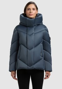 Tumesinine puffer-jope kõrge krae ja geomeetrilise tikandimustriga, sileda ja läikiva pinnaga. Varustatud küljetaskutega.