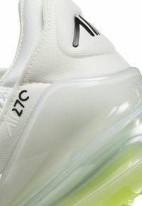 Sneaker bianca con tomaia in rete, dettagli in logo neri e suola trasparente che sfuma nel verde. Dettaglio di ammortizzazione notevole sul tallone.