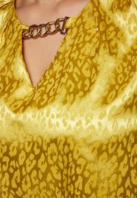 Yellow satin top featuring a leopard print pattern, deep V-neck, and a metallic chain accent at the neckline. Smooth texture.
