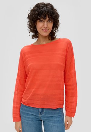 Haut long à manches en corail vif avec une texture à rayures horizontales, tissu léger, grand col et coupe décontractée, associé à un pantalon en denim bleu.