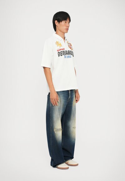 Fehér, rövid ujjú póló ing színes hímzéssel, oversized, fakó kék farmernadrággal párosítva, amely elkopott részletekkel és világosító hatásokkal rendelkezik.