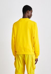 Felpa gialla con colletto rotondo e orli a costine, realizzata in materiale morbido, abbinata a pantaloni cargo gialli coordinati.