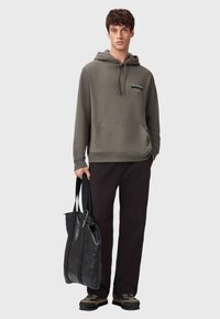 Szara bluza z kapturem, kieszenią z przodu, sznurkiem przy kapturze i detalem logo, w połączeniu z czarnymi spodniami oraz czarną skórzaną torbą na ramię. Całość uzupełniają casualowe buty.