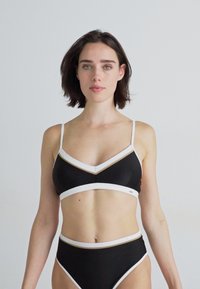 Set di bikini nero composto da un reggiseno triangolare con dettagli bianchi e dorati e un paio di slip a vita alta abbinati, realizzati in tessuto liscio.