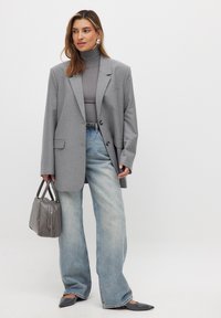 Grå skräddarsydd kavaj över en grå polotröja, i kombination med vida blå jeans. Tillbehör inkluderar en grå handväska och grå pumps med spetsig tå.