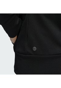 Schwarzer Sweatshirt mit strukturiertem unteren Saum, versehen mit einem kleinen, silbernen Globus-Logo an der Seite. Das Material wirkt glatt und leicht reflektierend.