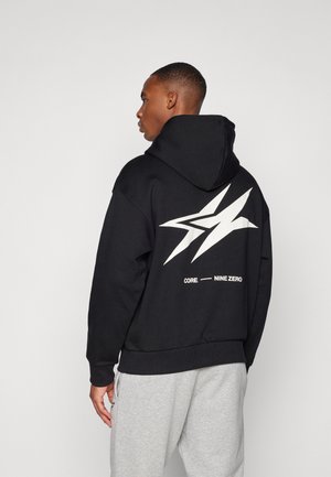 Black hoodie with a large white lightning bolt design on the back. Features elasticated cuffs and hem. Paired with gray sweatpants.
