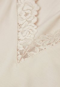 Tejido beis con un borde de encaje y patrones florales alrededor de un escote en forma de V; textura suave con un delicado acabados.