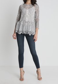 Grå spets peplumtop med långa ärmar och scalloptrim, tillsammans med mörka skinny jeans och silvriga ankarsremmar.