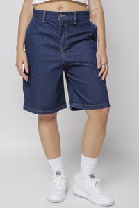 Blå denimshorts med en avslappet passform, synlig søm og rullkant, sammen med hvite sneakers og sokker.