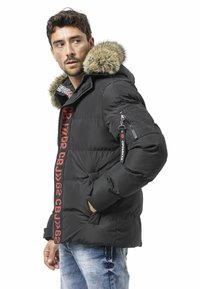 Schwarze Steppjacke mit Kapuze aus Kunstpelz, rotem Markenlogo am Reißverschluss und Seitentaschen. Verfügt über eine Reißverschlusstasche am Ärmel.