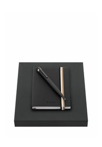 Carnet noir avec bande élastique blanche et beige, marqué « Boss », et stylo noir assorti sur boîte cadeau noire.