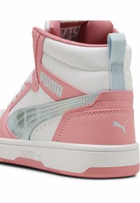Kõrged sneakerid, mis on valmistatud roosa ja valge sünteetilisest nahast, metalliliste hõbedaste aksentidega ning tekstureeritud võrgusisuga. PUMA logo on nähtaval.
