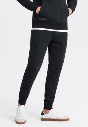 Svarta träningsoveraller med en smal passform, elastisk midja och sidofickor, i kombination med vita sneakers med svart hälaccent.