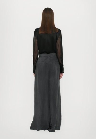Blusa nera trasparente a maniche lunghe abbinata a pantaloni grigi scuri a vita alta e a gamba larga. Tessuto fluido e morbido con una leggera texture.