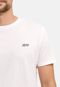 Hvit bomulls t-skjorte med rund hals og korte ermer, med "JEFF" trykt i svart på venstre brystområde.