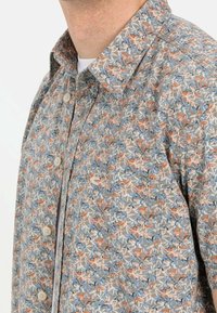 Korteblouson met een bloemenpatroon in oranje, blauw en crèmekleurig op een lichtgrijze achtergrond. Knopsluiting en zachte stofstructuur.