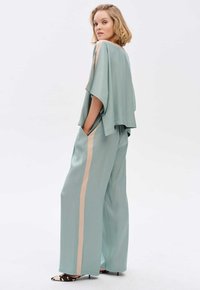 Miętowa bluzka z szerokimi rękawami i bocznymi rozporkami, zestawiona z dopasowanymi luźnymi spodniami z beżowym pasem po boku. Teksturowana tkanina.