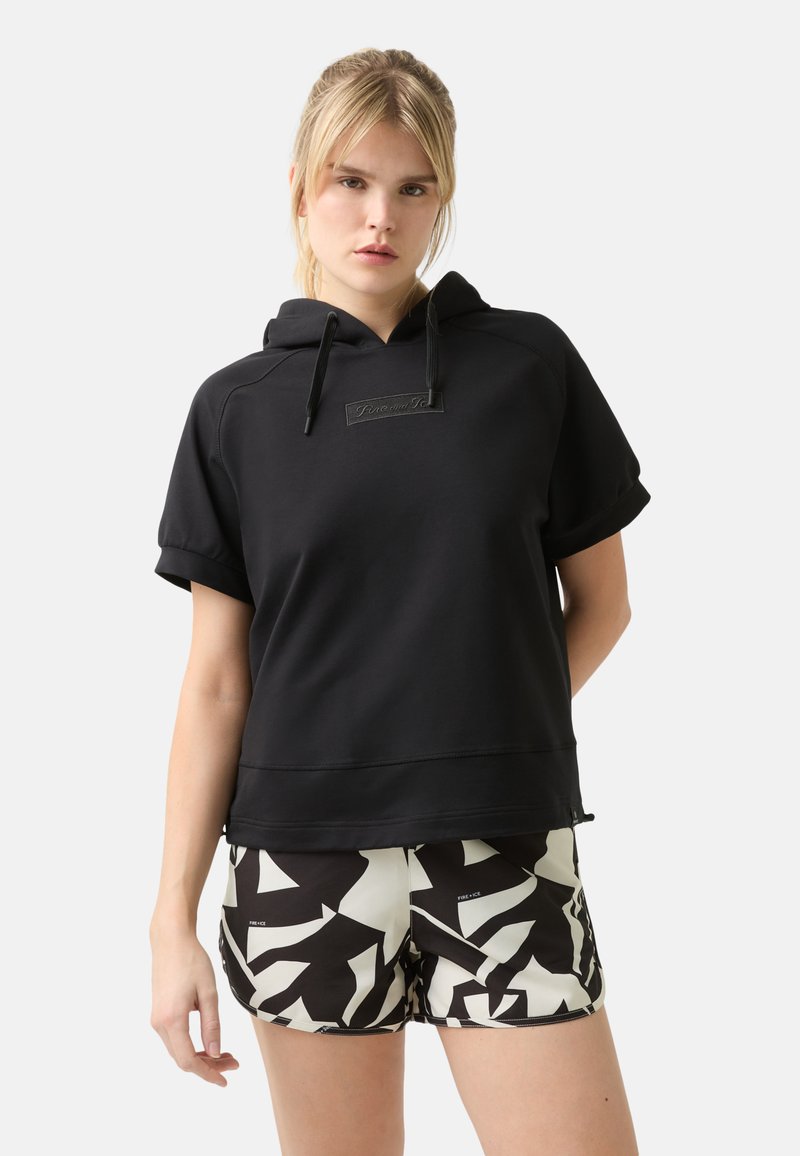 Schwarzer Kurzarm-Hoodie mit einer Fronttasche, ausgestattet mit einem strukturierten Logo-Patch und Kordeln. Kombiniert mit gemusterten Schwarz-weiß-Shorts.