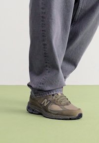 Grå New Balance-sneakers har en blanding av mesh og semsket skinn, med mørke aksenter og en polstret såle, paret med grå, løstsittende bukser.