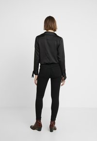 Black satin blouse with long sleeves, featuring a smooth texture and tied cuffs, paired with black slim-fit jeans and brown ankle boots.