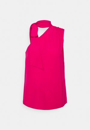 Kirkkaan pinkki hihaton paita, jossa suuri rusetti epäsymmetrisessä pääntiessä, valkoista taustaa vasten esitettynä.