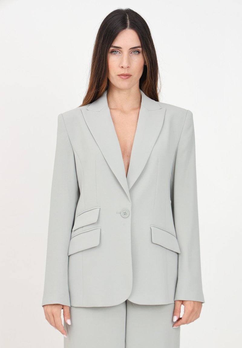 Blazer grigio chiaro con spalle imbottite, rever a punta, chiusura con un bottone e due tasche frontali angolari. Tessuto liscio e sartoriale.