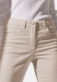 Beige gestreepte high-waisted jeans met vijf zakken en een metalen knoopsluiting, met een gladde textuur en een slanke pasvorm.
