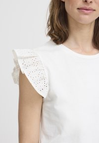 T-shirt en coton blanc avec des manches en dentelle blanche brodée. Encolure ronde simple et coupe décontractée. Texture lisse tout au long.