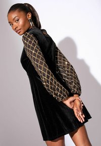 Fekete bársony ruha puffos átlátszó ujjal, arany gyémántmintával, testhezálló felső résszel és bővülő szoknyával. Simás textúra.