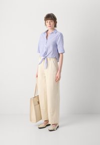 Lys blå og hvitstripet kortermet skjorte knyttet i livet, kombinert med kremfargede vide bukser, beige lettpustende sko og en beige tote-veske.
