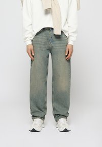 Faded light blue wide-leg jeans with a loose fit, featuring a classic five-pocket design and subtle distressed detailing. Worn with a white sweater.