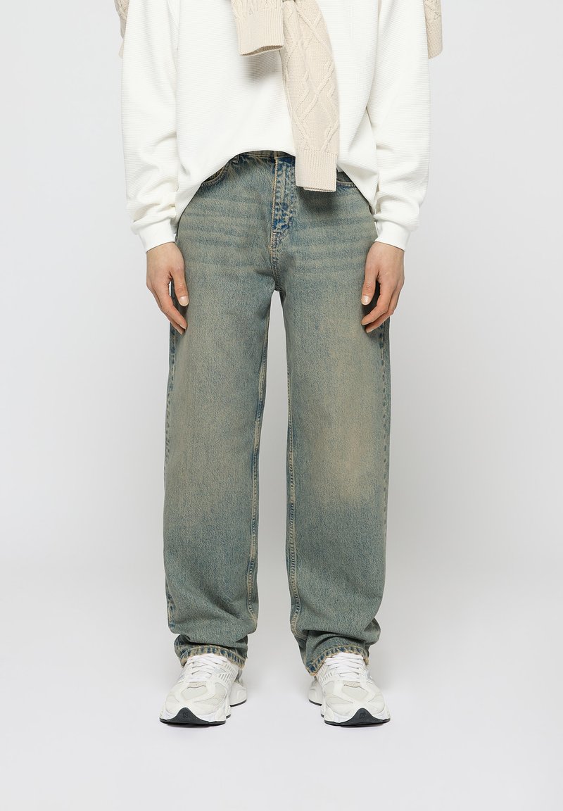 Faded light blue wide-leg jeans with a loose fit, featuring a classic five-pocket design and subtle distressed detailing. Worn with a white sweater.
