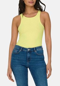 Top sin mangas amarillo de canalé con escote redondo, combinado con pantalones vaqueros de denim azul de tiro alto con puños, que presentan bolsillos delanteros y cierre de botón.