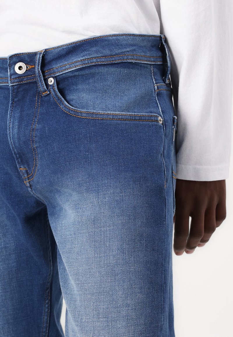 Blaue Jeans aus Denim mit einem ausgebleichten Finish, Fünf-Taschen-Design, kontrastierender orangefarbener Naht, Metallknopfverschluss und strapazierfähiger Stofftextur.
