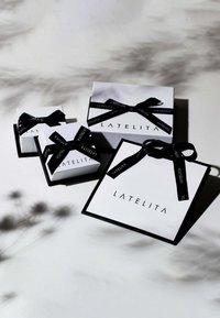 White gift boxes of varying sizes, decorated with black satin ribbons and printed logos. Simple, elegant design with stark color contrast.