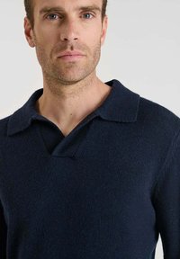 Suéter de punto azul marino con diseño de cuello y escote en V, tejido texturizado y corte relajado. Sin logotipos ni patrones visibles.
